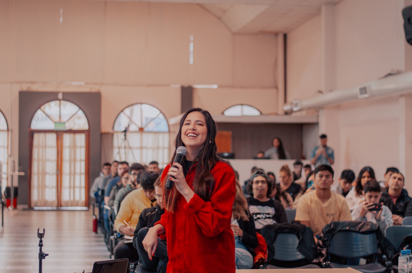 Una donna parla al microfono a un pubblico seduto in una sala.