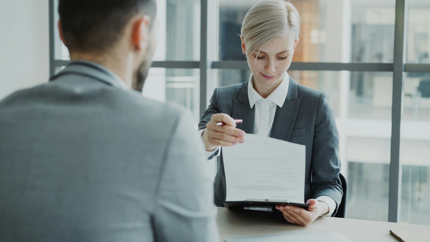 Imprenditrice offre documento e penna a un cliente in ufficio.