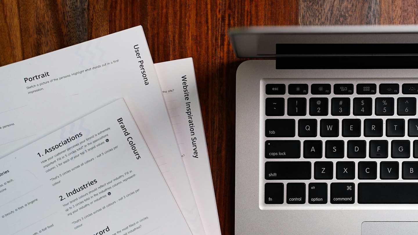 Computer portatile e documenti su una scrivania di legno scuro.
